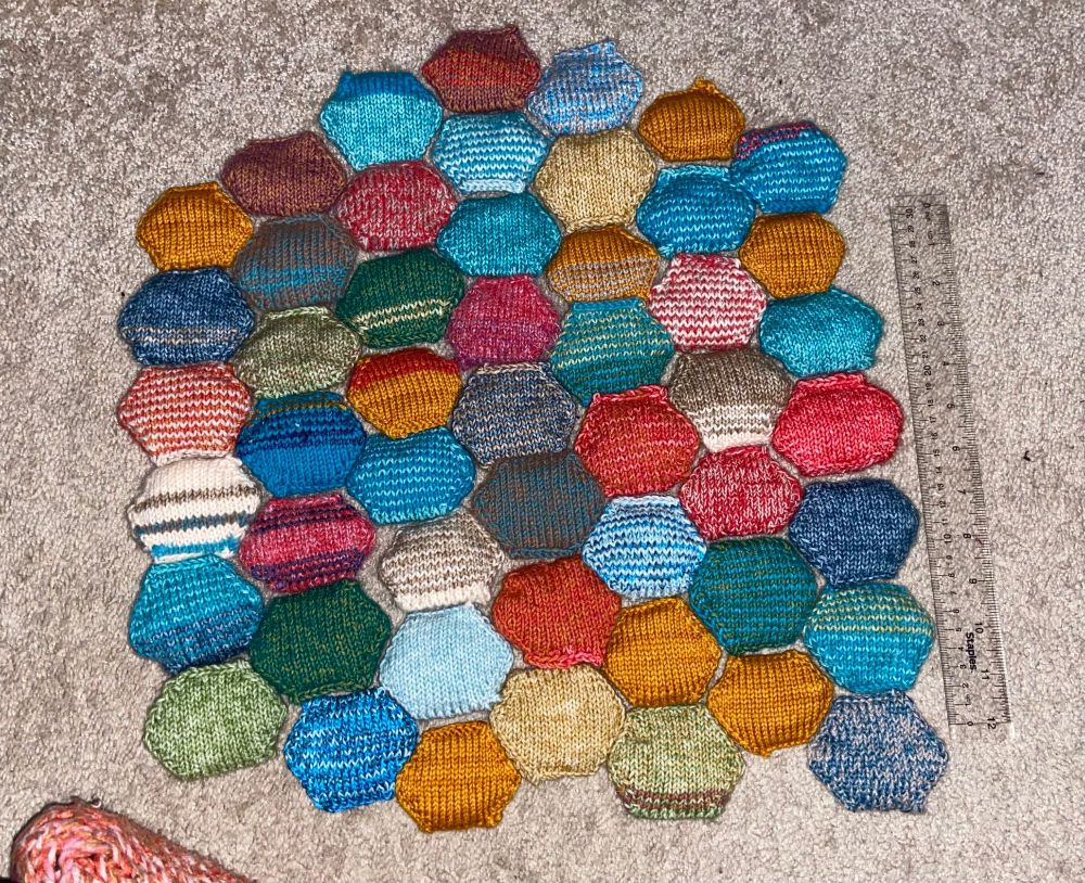 51 solid and striped hexagonal knitted puffs in a variety of colors, next to a ruler