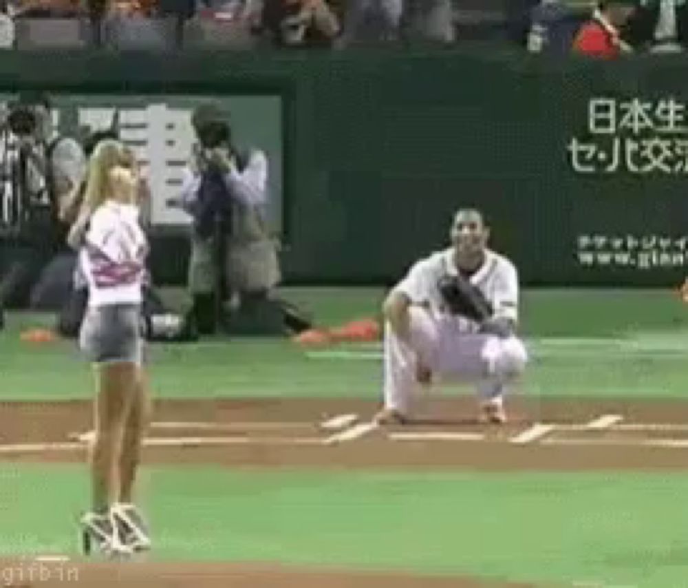 a woman is standing on a baseball field next to a man kneeling on the mound .