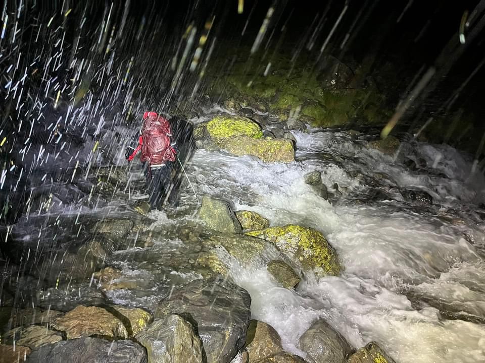 Mountain rescue team member in a red waterproof jacket (I really hope it was waterproof), in torrential rain, at night, crossing a stream in spate.