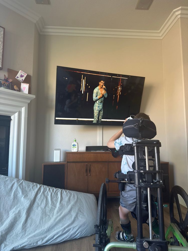 A white, 8 year old boy is pictured in a gait trainer watching Benson Boone performing Bohemian Rhapsody at Coachella
