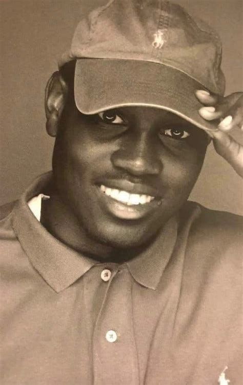 Ahmaud Marquez Arbery in a septia toned picture wearing a polo shirt and hat, smiling.