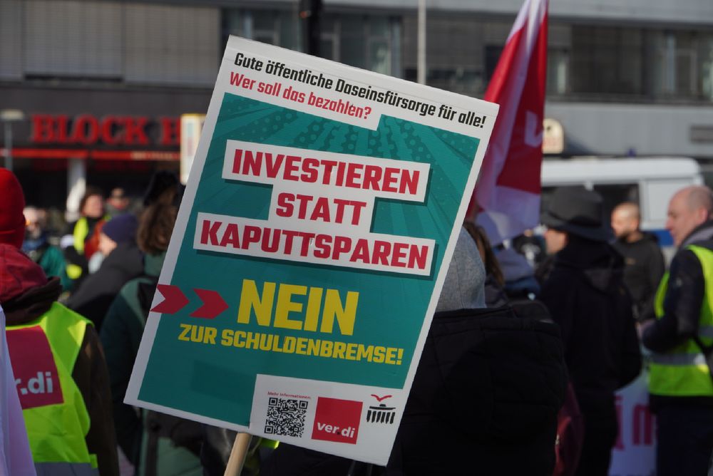 Schild von ver.di mit der Aufschrift: "Gute öffentliche Daseinsfürsorge für alle. Wer soll das bezahlen? Investieren statt kaputtsparen."