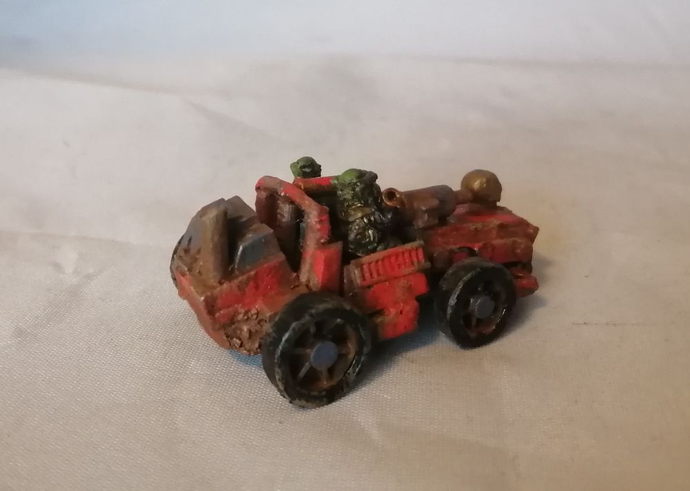 A scratchbuilt toy car in red with a pair of ork crew. Its got a machine gun, and a lot of rust. Rear angled view.