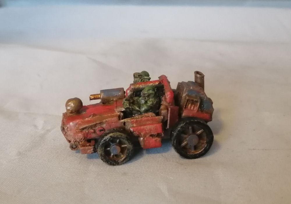 A scratchbuilt toy car in red with a pair of ork crew. Its got a machine gun, and a lot of rust. Driver side view.