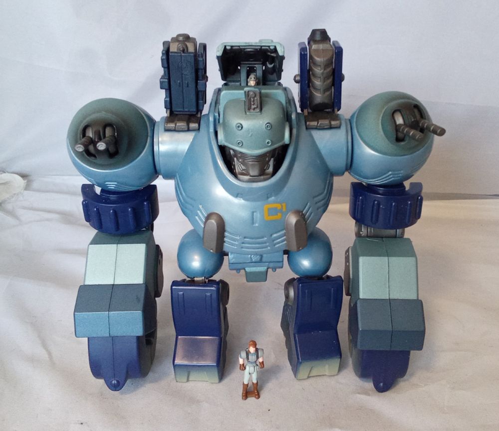 A blue, steampunky sort of robot with proportions like a gorilla, and shoulder turrets. Front view, with mini-figures, and cockpit open.