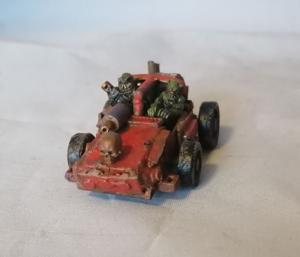 A scratchbuilt toy car in red with a pair of ork crew. Its got a machine gun, and a lot of rust. Front view.
