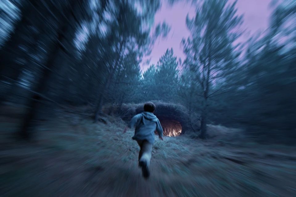 A dynamic tracking shot of a boy sprinting through a dense pine forest, motion blur sweeping past, a glowing cave ahead, dusky purple sky glowing behind him, wind in his hair, urgency and freedom in every stride. --ar 3:2 --v 7