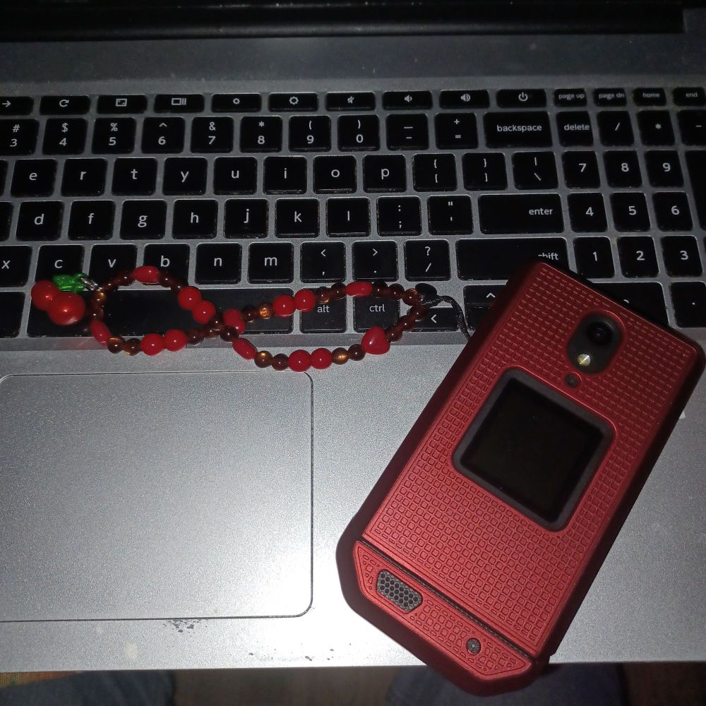 Red flip phone with cherry phone charm sitting on a laptop keyboard