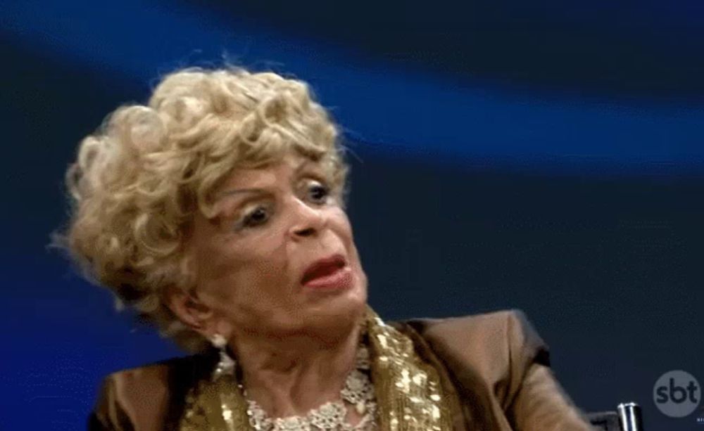 a woman wearing a wig and a gold jacket is making a funny face