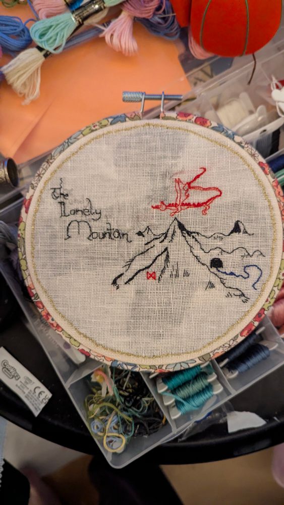 An embroidery piece of The Lonely Mountain, with a little red Smaug flying over. 