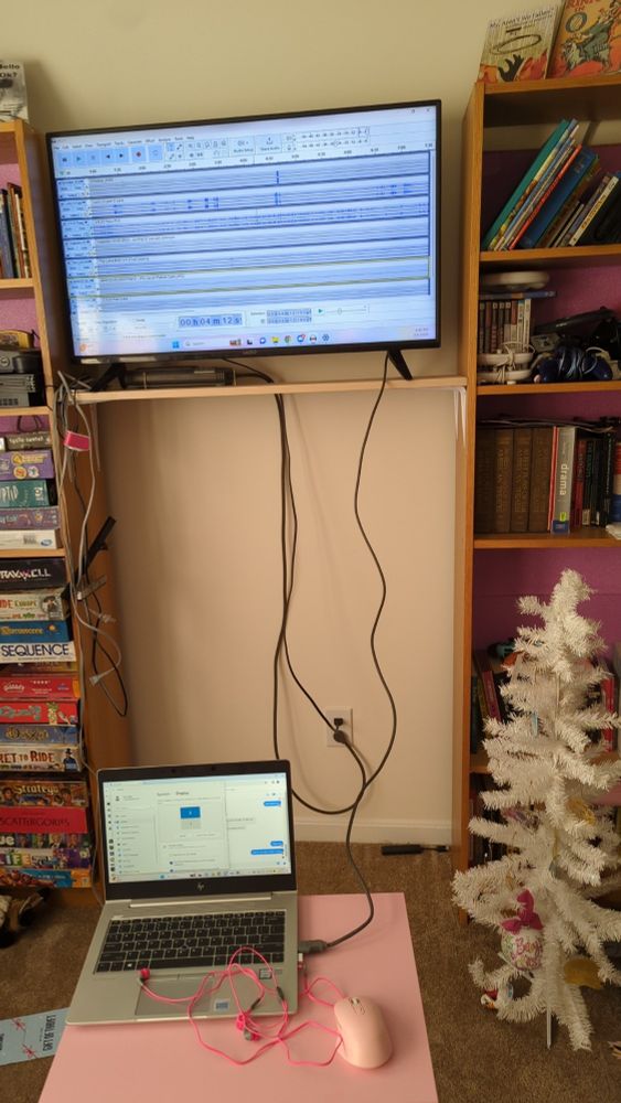 A television sits on a shelf, connected to a laptop by an HDMI cable. On the television monitor, you can see several lines of audio in the program Audacity.