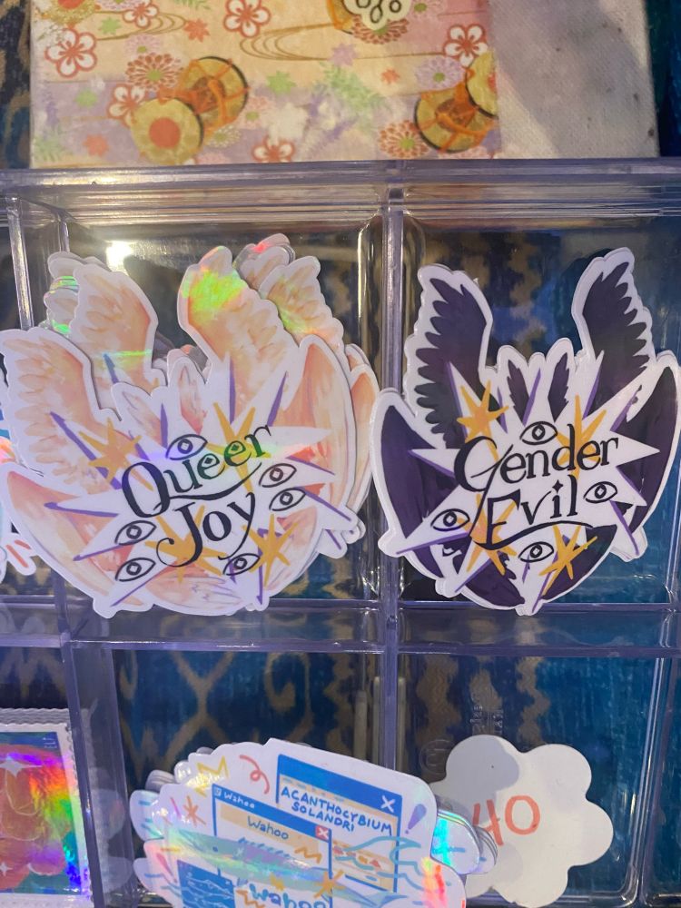 Photo of my stickers, biblically accurate angels with typography queer joy and gender evil. Gender evil has less stocks vs the queer joy sticker