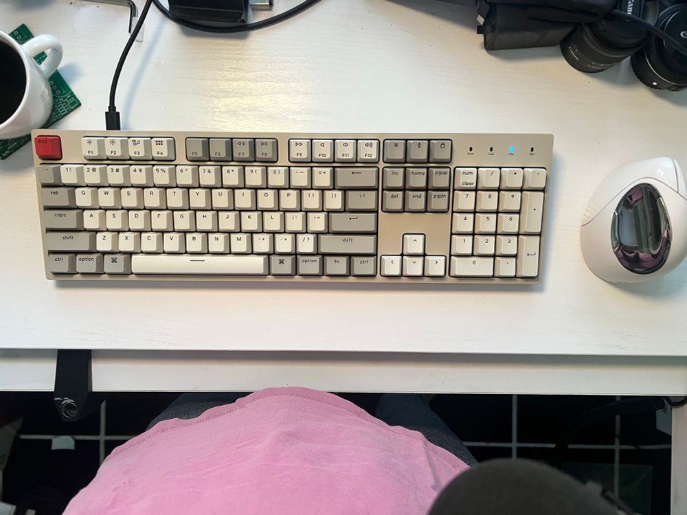 Overhead view of a desktop with a wired mechanical keyboard with a retro color scheme and a white Bluetooth vertical mouse to the right
