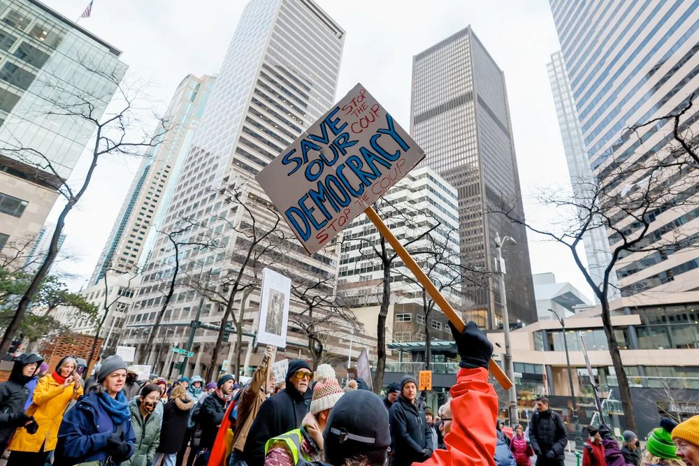 People rally outside the Federal Building protesting federal funding freezes Feb. 5 in Seattle. A protest sign says, "Save Our Democracy. Stop the Coup."(Jennifer Buchanan / The Seattle Times)
