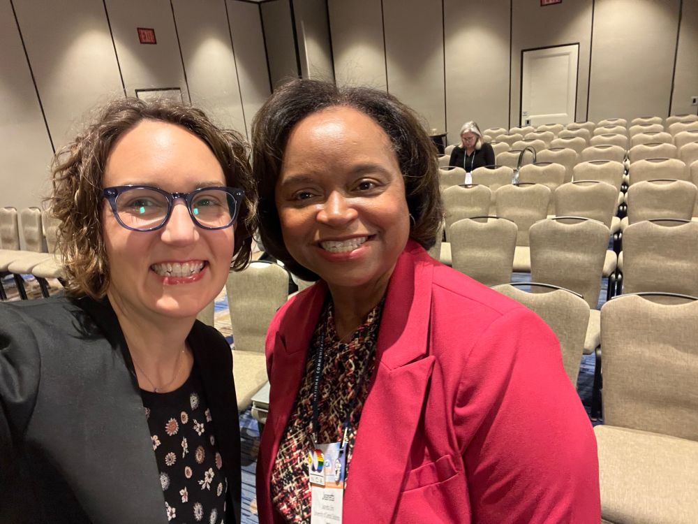 Lindsay Currie wearing a black suit taking a selfie with Jeanetta Sims in hot pink. 