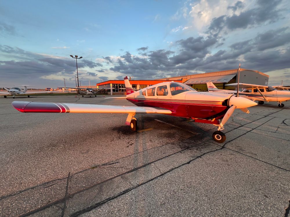 A red and white Piper Arrow aircraft bathed in golden light as it sits on an airport apron.