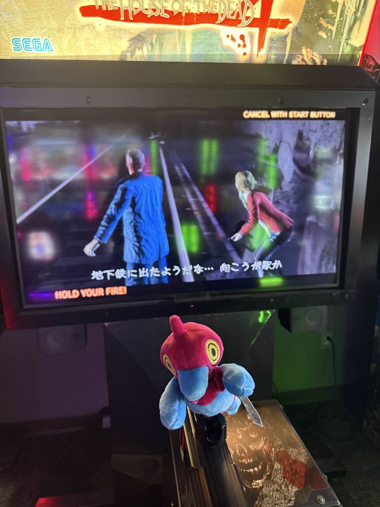 A porygon z plush with a bowtie (which Kirm has named Pivolo, go figure) sat atop a plastic gun pointed at the screen of a 'The House of the Dead 4' cabinet. The game is currently using JPN captions.