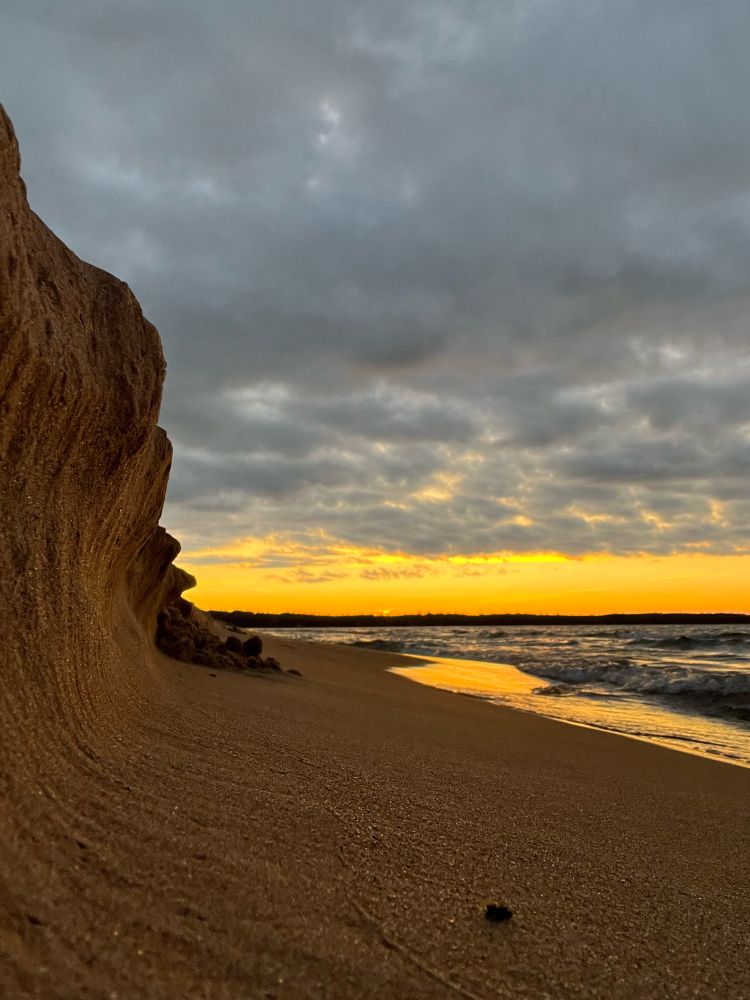 A forced perspective shot to make a small, sandy cliff appear larger. The sun is setting in the background.