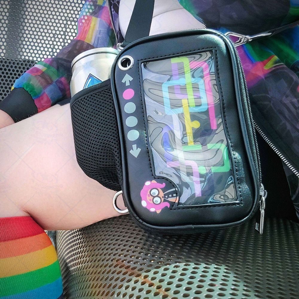 My Essentials Ita Bag in the Octo Expansion variant. It's hanging off the side of a person like a crossbody bag. The person is sitting down at a train stop bench. A tacticooler cup is being held in a mesh pocket.