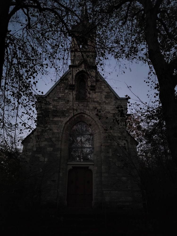 Eine Kapelle im Wald, der Himmel ist schon sehr dunkel. 