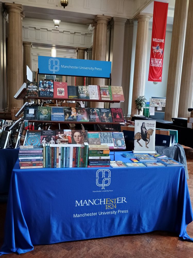 A photograph of the Manchester University Press books exhibition table at Leeds International Medieval Congress, a banner for the Medieval Studies Digital collection, Renaissance Skin and Refashioning the Renaissance are prominently displayed among the other Manchester University Press titles.