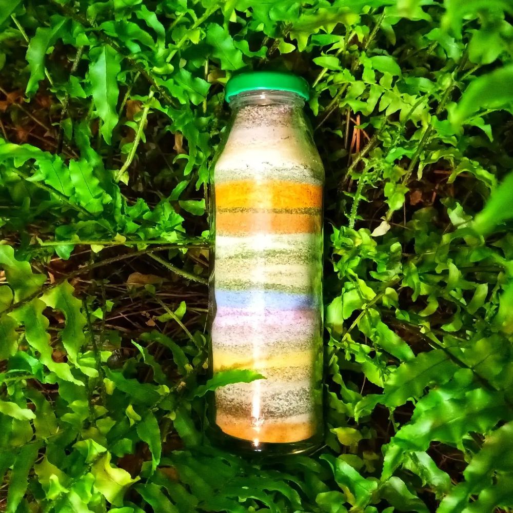 Inmitten einer grünen Pflanze liegt eine Glasflasche mit verschieden gefärbten Schichten des im Post beschriebenen Salzes.