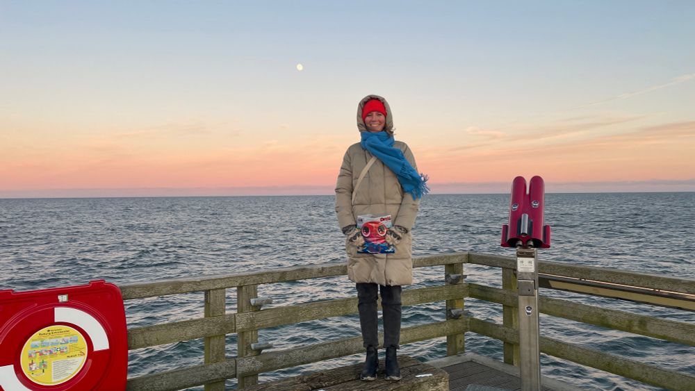 Person auf einem Steg am Meer vor dem Horizont mit Mond 