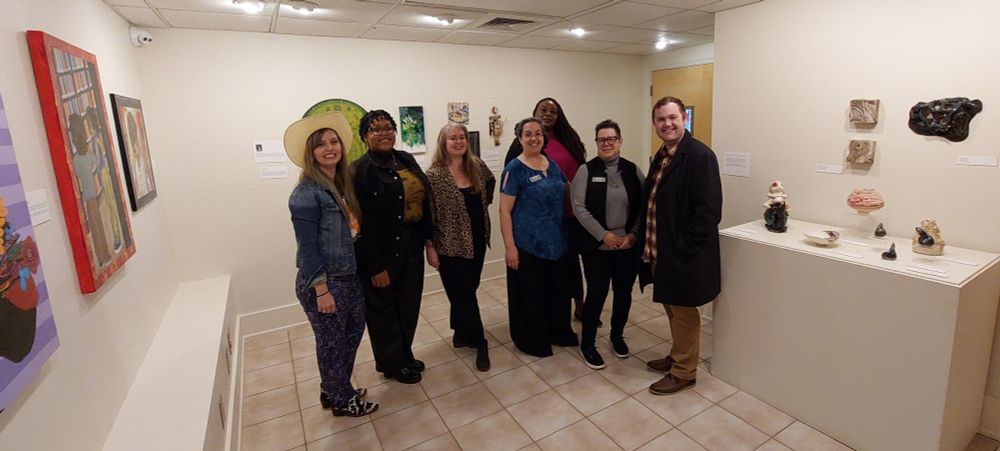 The art educators, whose work is on display at the museum until the end of March. 

7 of the 8 art educators currently on display, pose where you get a glimpse of 4 of the displays.