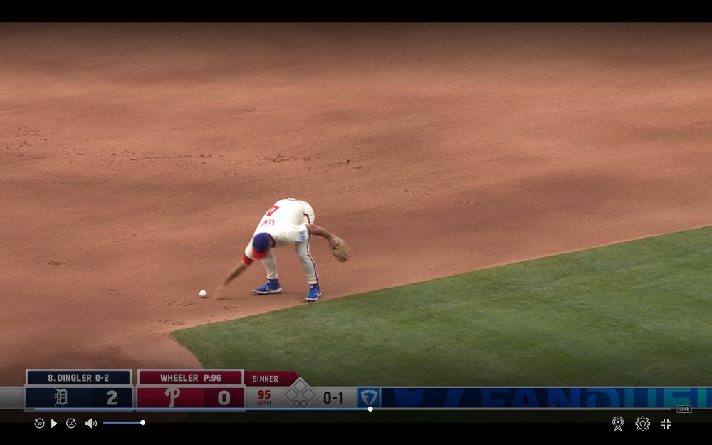 A Phillies infielder flatfooted reaching for a ball on the ground but it is comically just beyond his grasp