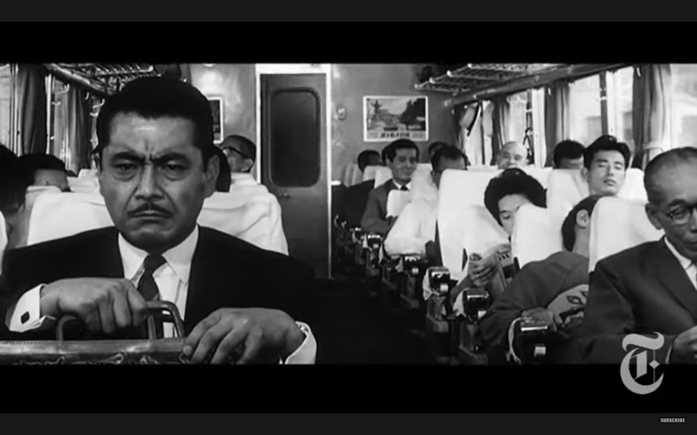 The shot cuts to a straight ahead shot of an incredibly tense and serious, seated on the train with a briefcase full of ransom money on his lap. The two cops can be seen looking at him admiringly in the background.