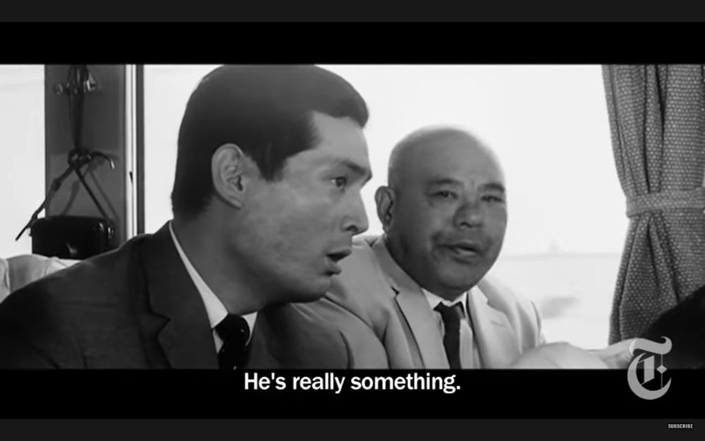 From Kurosawa's HIGH AND LOW, two men in suits sitting next to each other on a train speaking. The younger man, Inspector Tokura, is looking ahead at someone in the car offscreen, saying, "He's really something."