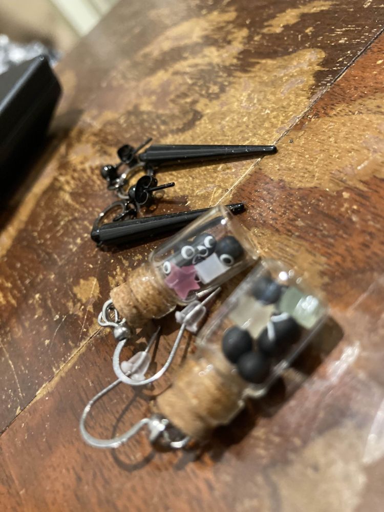 Two sets of earrings! One is a set of little jars full of little soot balls with eyes and star shaped crystals; the other is a set of long black spikes