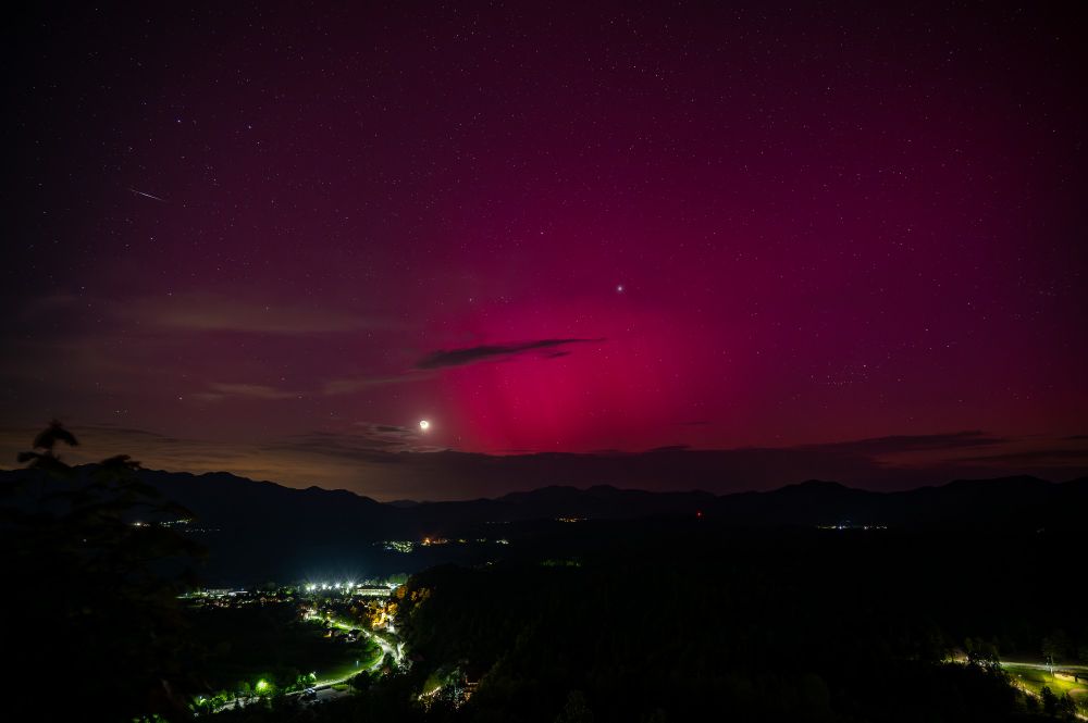 A red aurora visible from Slovena in May 2024 with a moon low on the horizon and a meteor in a super left corner.