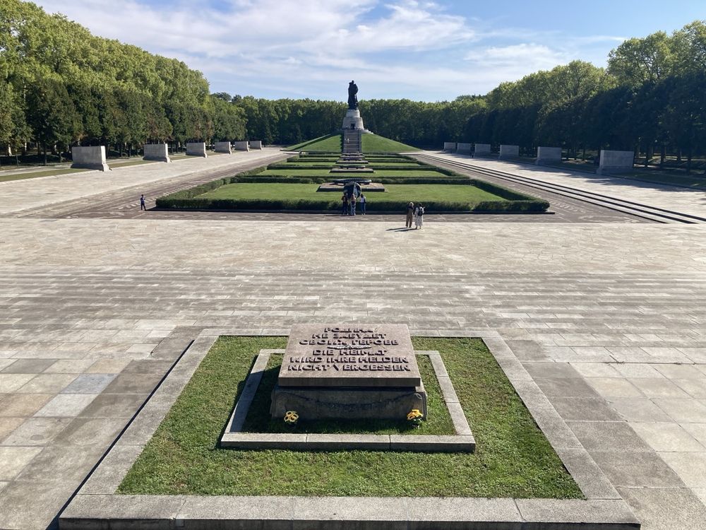 View over the Soviet War Memorial in Treptower Park, Berlin. In the foreground a bronze plaque reads "the homeland will not forget its heroes" in Russian and German. In the background is the monumental statue of "The Liberator".
