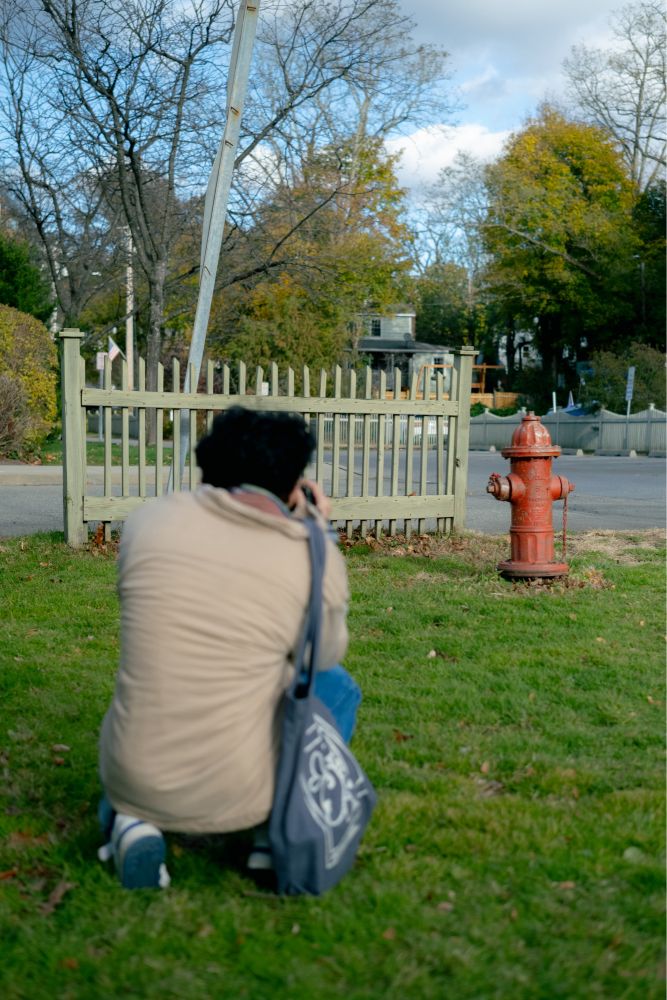 young man kneeled down with his back to the camera as he takes a picture of a red fire hydrant