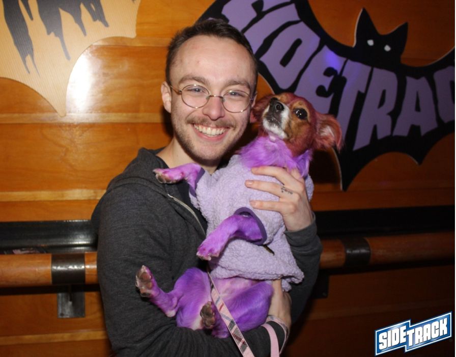 Rocking a five head with a short hair cut, he has a gold wire rim glasses and a mustache over a smile that says, “he probably smokes too much.” holding my dog, Girlfriend, who is dyed purple and dressed as the Princess Diana beanie baby. 
