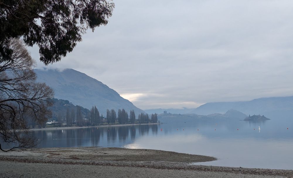 Photo of a lake under a heavily clouded sky, distant mountains blurring into the horizon