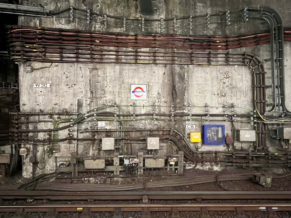 A wall at Aldgate Station of the London Underground covered with  a busy maze of cables, conduit and junction boxes
