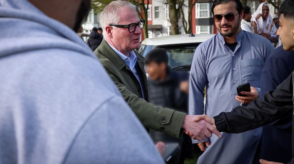 Two people shaking hands while other people look on during a mass congregation.