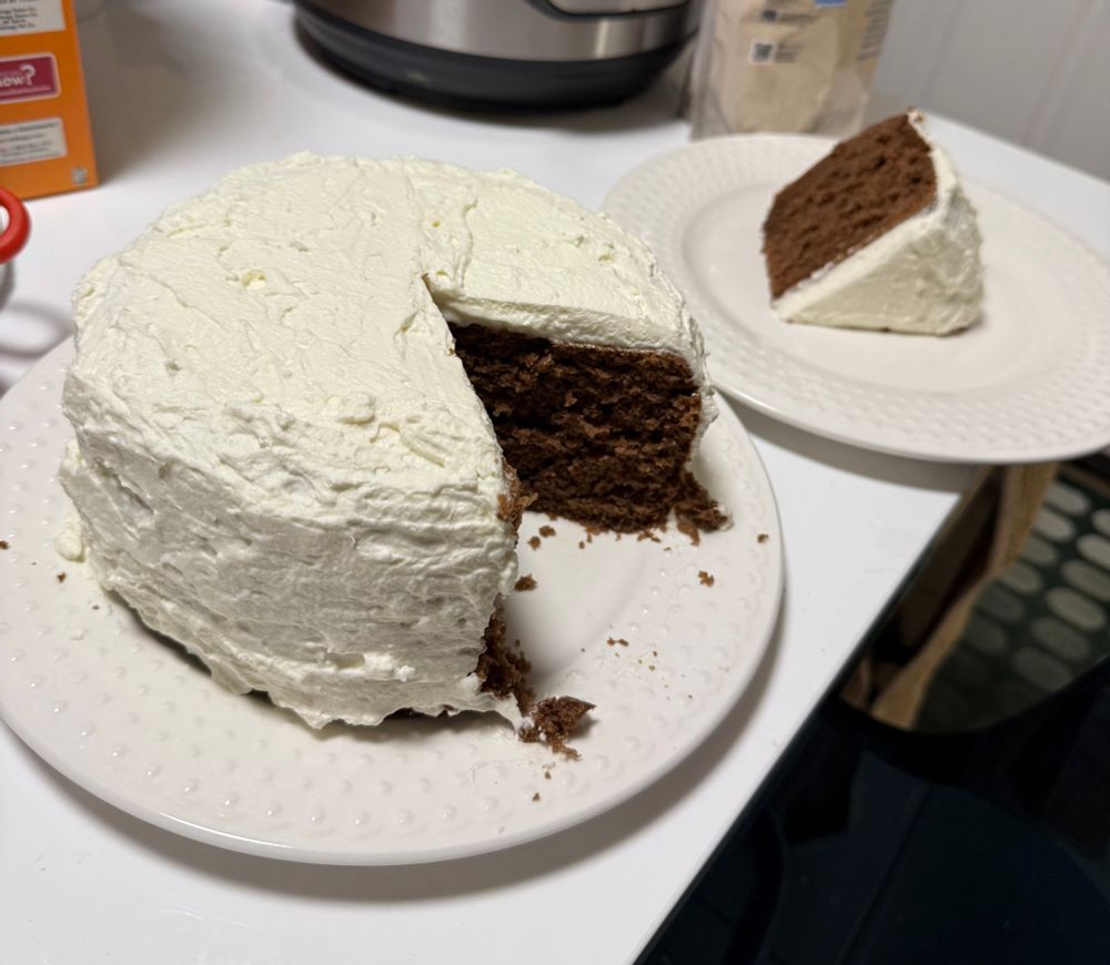 A picture of an approximately 4 inch thick slice of chocolate cake with white whipped cream icing covering it. A slice of the cake is on its side behind it.