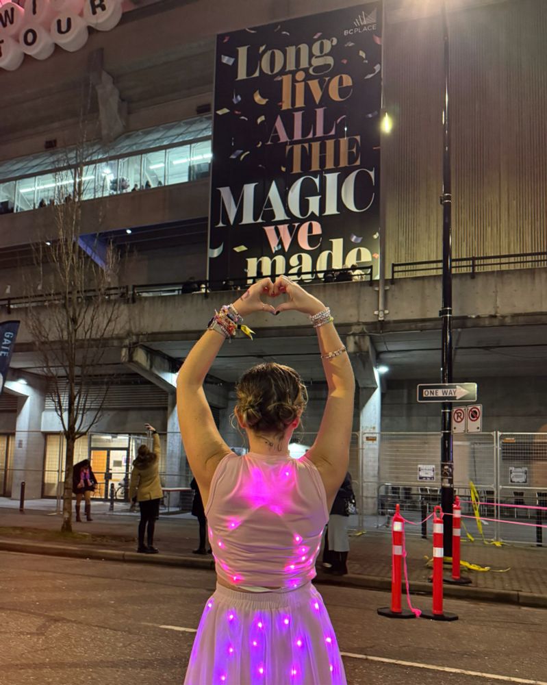 Girl wearing a light up pink dress holding heart hands outside of the Eras Tour in Vancouver 