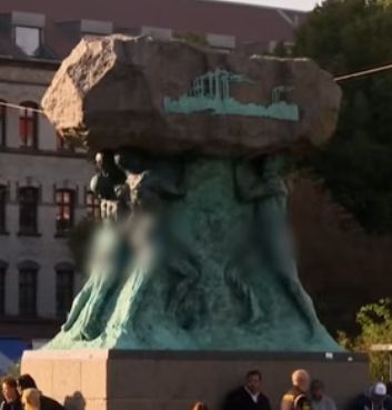An unknown statue of a few people holding up a large rock. Probably in a city center in Sweden.