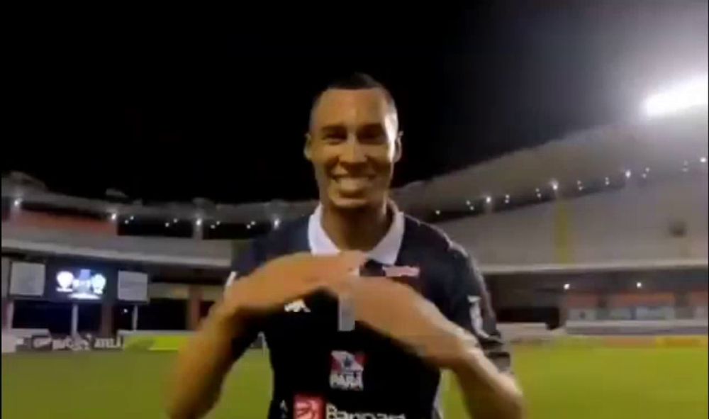 a soccer player is smiling and making a heart shape with his hands on a soccer field .