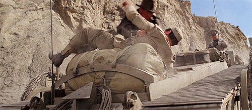 Indiana Jones (Harrison Ford) punching a Nazi on the back of a tank in a desert canyon. 