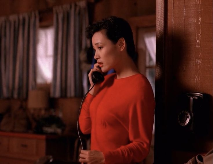 a still of Joan Chen as Josie from Twin Peaks calling into a black rotary phone in a wooded cabin-style house. she's wearing a red sweater. 