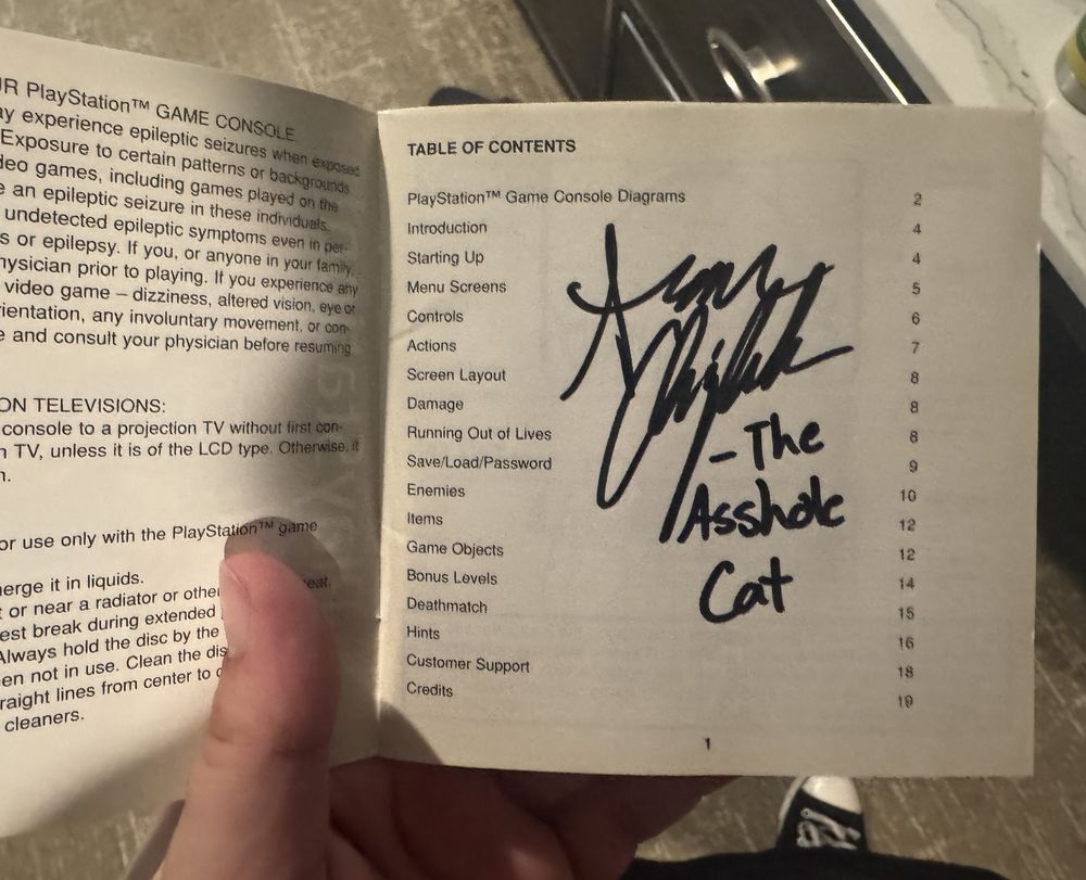 The inside of the "Bubsy 3D" game manual, with Sean Chiplock's signature and "-The Asshole Cat" written on the center of the page.