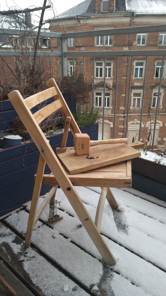 Klappstuhl aus hellem Holz, auf der Sitzfläche liegt ein Schneidbrett, darauf ein Holzhammer.