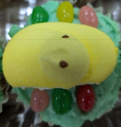 A yellow Peep sits atop a green frosted cupcake. Three jelly beans on either side give the impression of a jeweled throne.