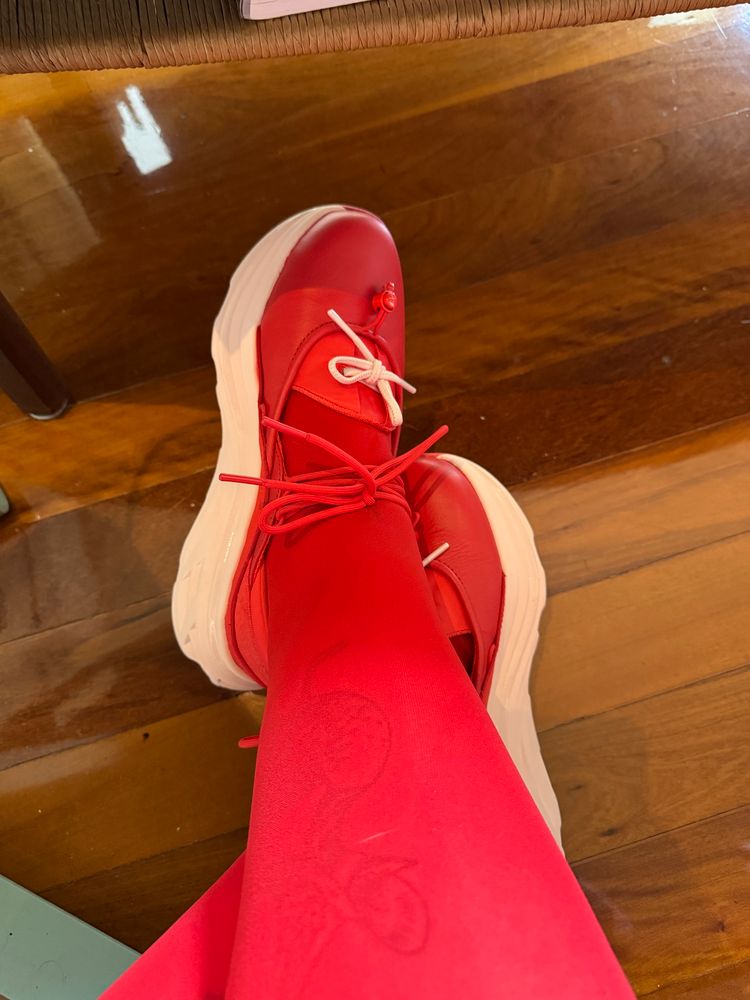 A photo of red stockinged legs wearing Hoka’s red and pink Bondi Mary Janes 