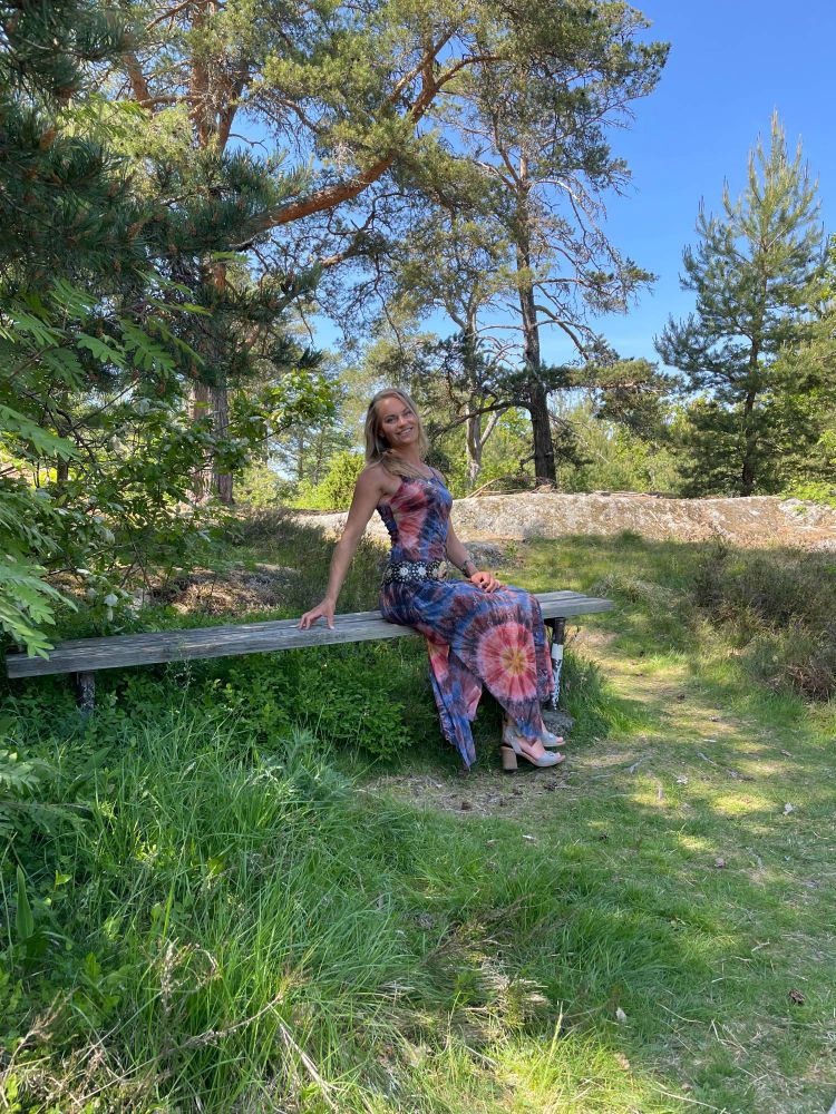This is a picture of me in a purple and pink dress. I'm sitting on a bench in the forest.